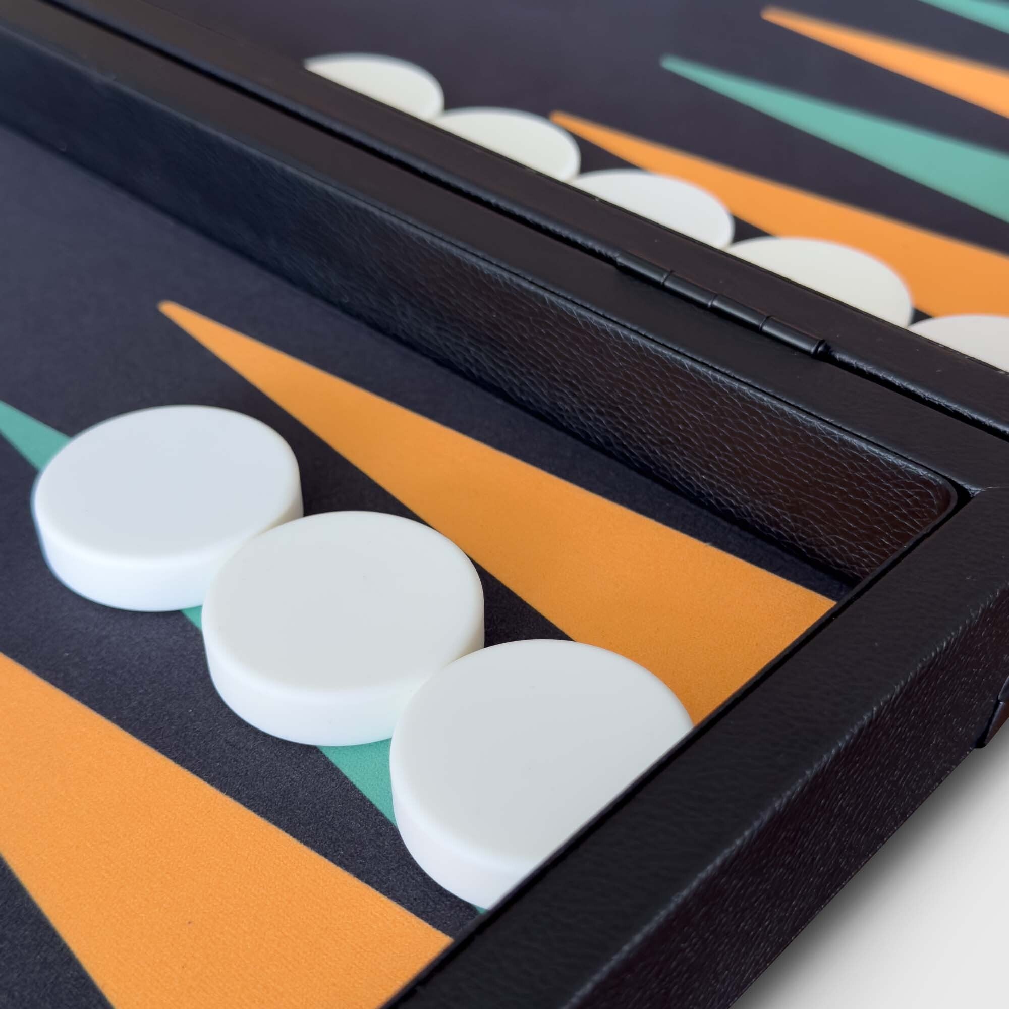 Close-up of a backgammon board with a black leather frame, orange and teal geometric points, and white checkers. From the Nova backgammon board.