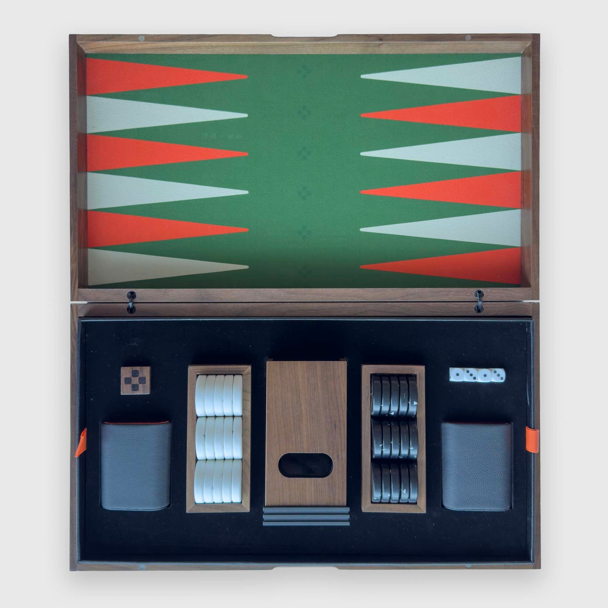 An open wooden "PRIME" backgammon set displayed against a light gray background. The top half shows the green playing field with red and white triangles, and the bottom half shows the black game box interior with dice, checkers, and storage pockets.