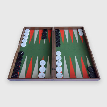 An open "PRIME" wooden backgammon board with a green playing field, orange and white triangular points, and black and white checkers, photographed from above on a light gray background.